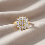 Goldener Luxus-Ring mit Blumenmotiv liegt auf weichem beigen Stoff, Detailansicht der hochwertigen Zirkonia-Fassung.