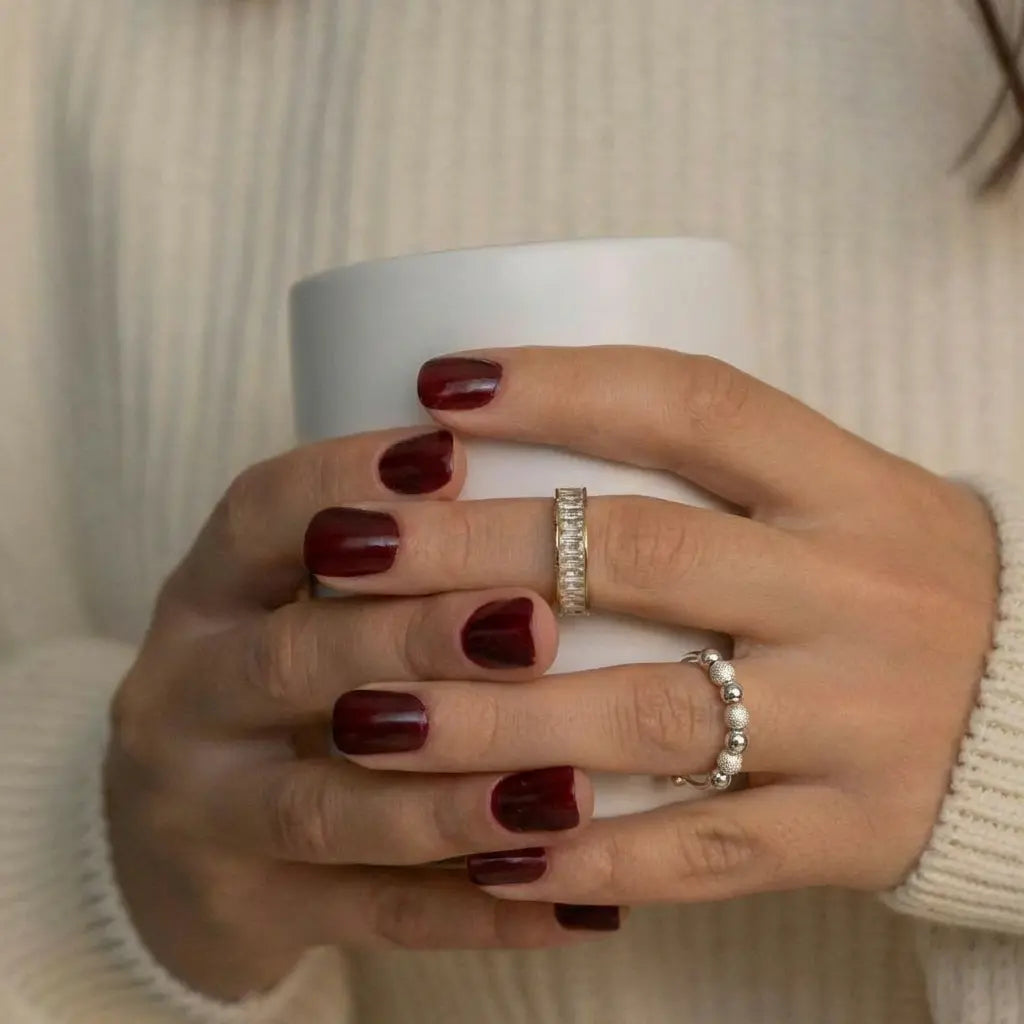 Frau mit roten Nägeln hält eine weiße Tasse und trägt den dezenten Nivia Perlenring am Ringfinger als schickes Accessoire.