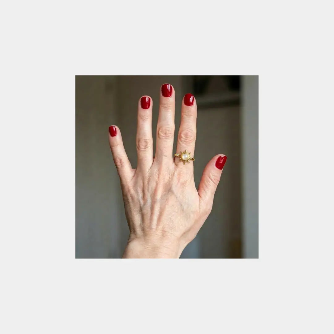 Gepflegte Hand mit rotem Nagellack trägt goldenen Aurelia Spinner Ring, Symbol für überwundenes Nägelkauen und innere Ruhe.