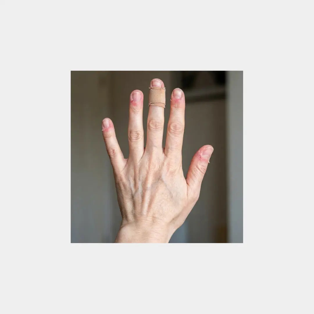 Hand mit Pflaster am Mittelfinger und eingerissener Nagelhaut, typische Anzeichen von Dermatillomanie (Skin Picking) und nervösem Nägelkauen.